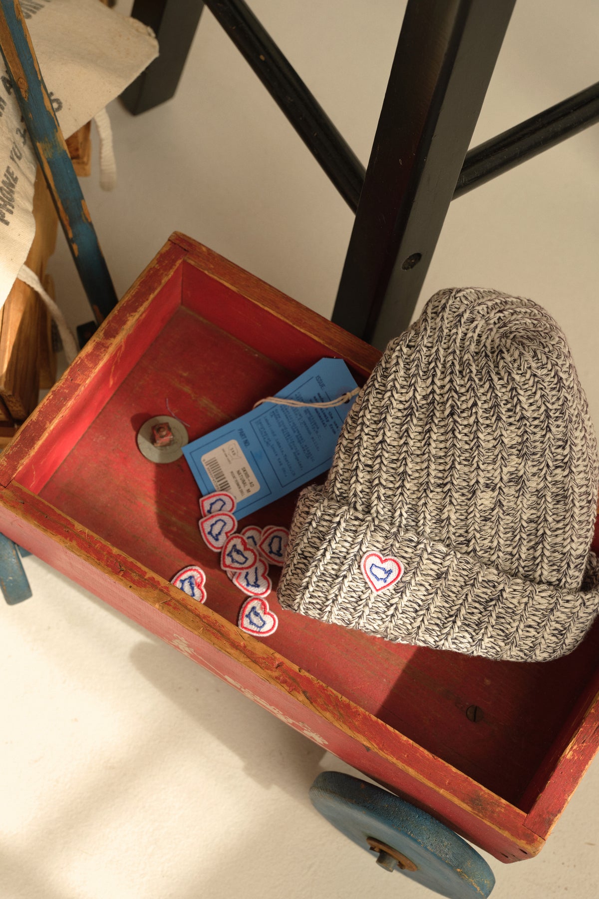 Light heather knit beanie with red heart logo patch in a tray