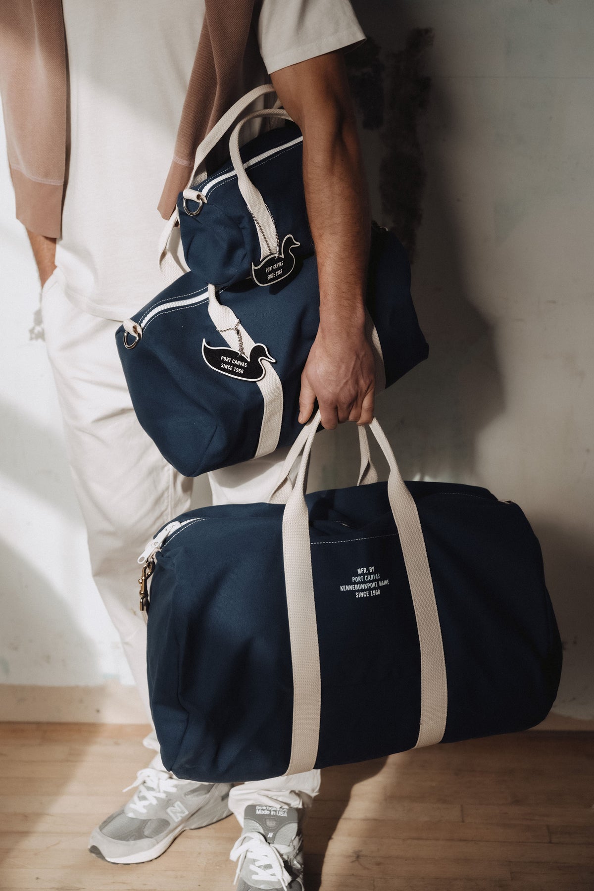 Navy duffel bag with cream stripes, plus smaller bag, carried by person