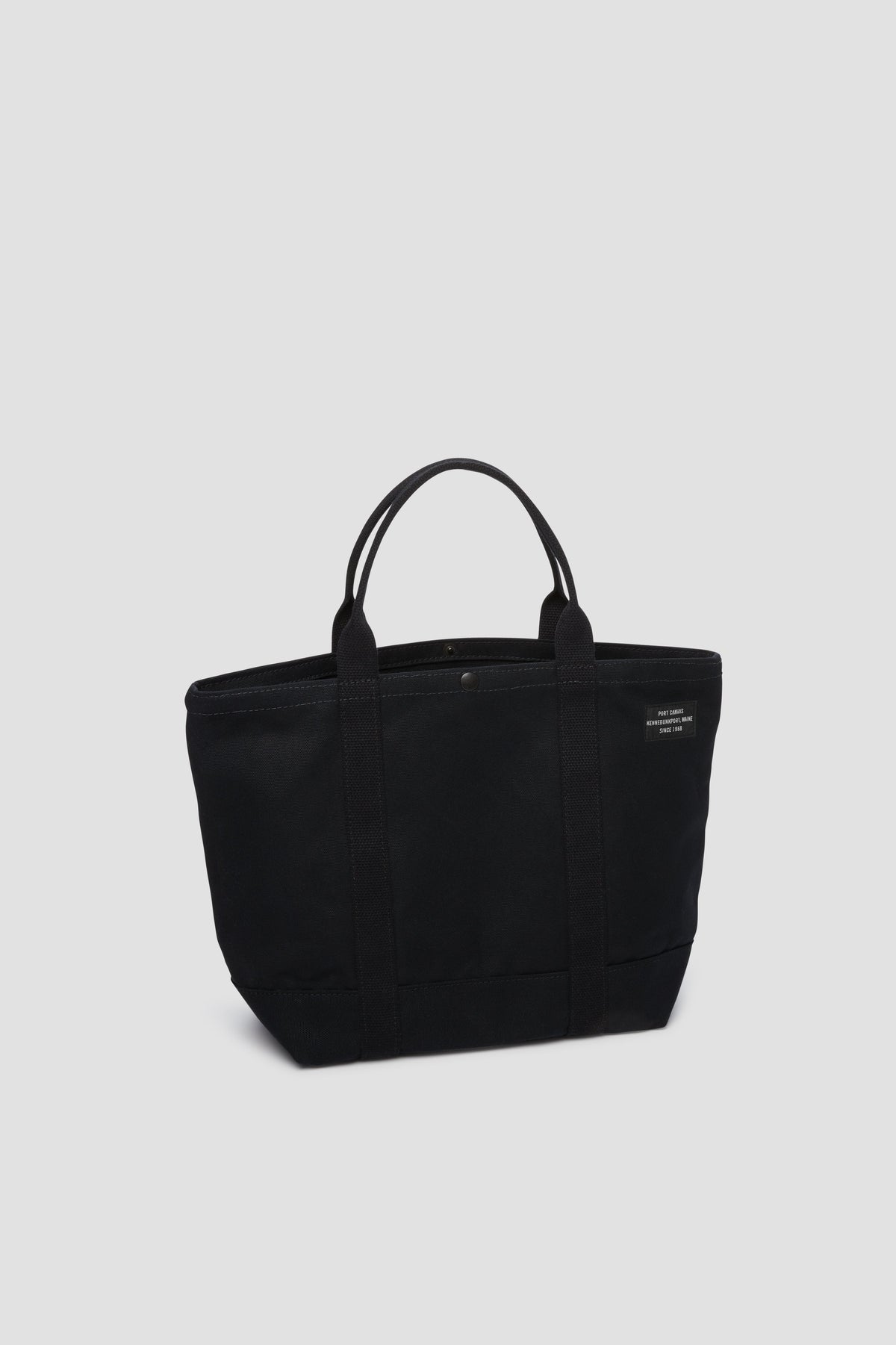 Black canvas tote bag with long handles and small front pocket detail