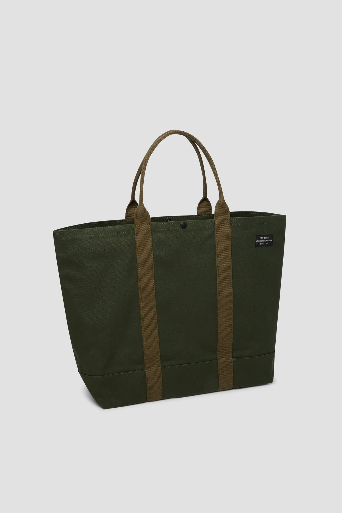 Olive canvas tote bag with top button, short handles, and front patch logo.