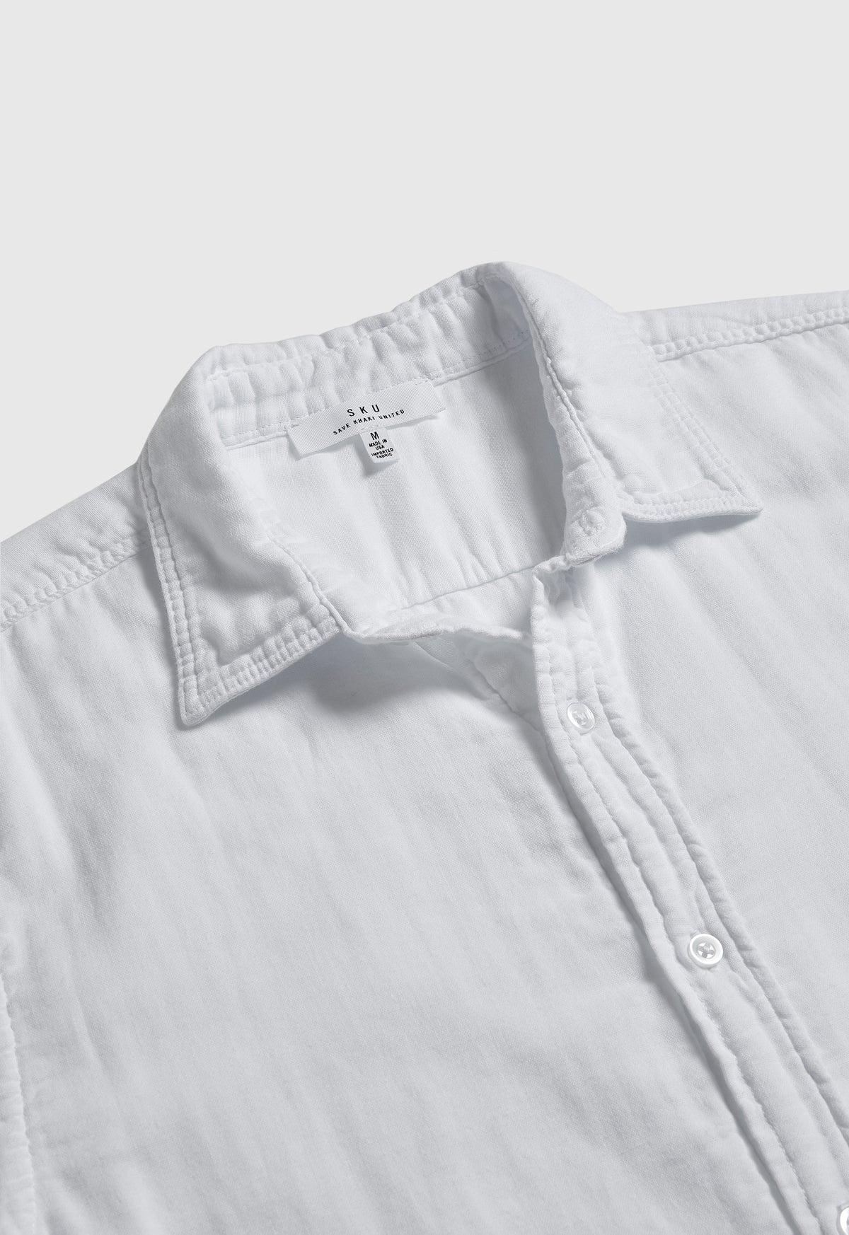 Men's white button-up shirt detail: pointed collar, button placket, chest yoke