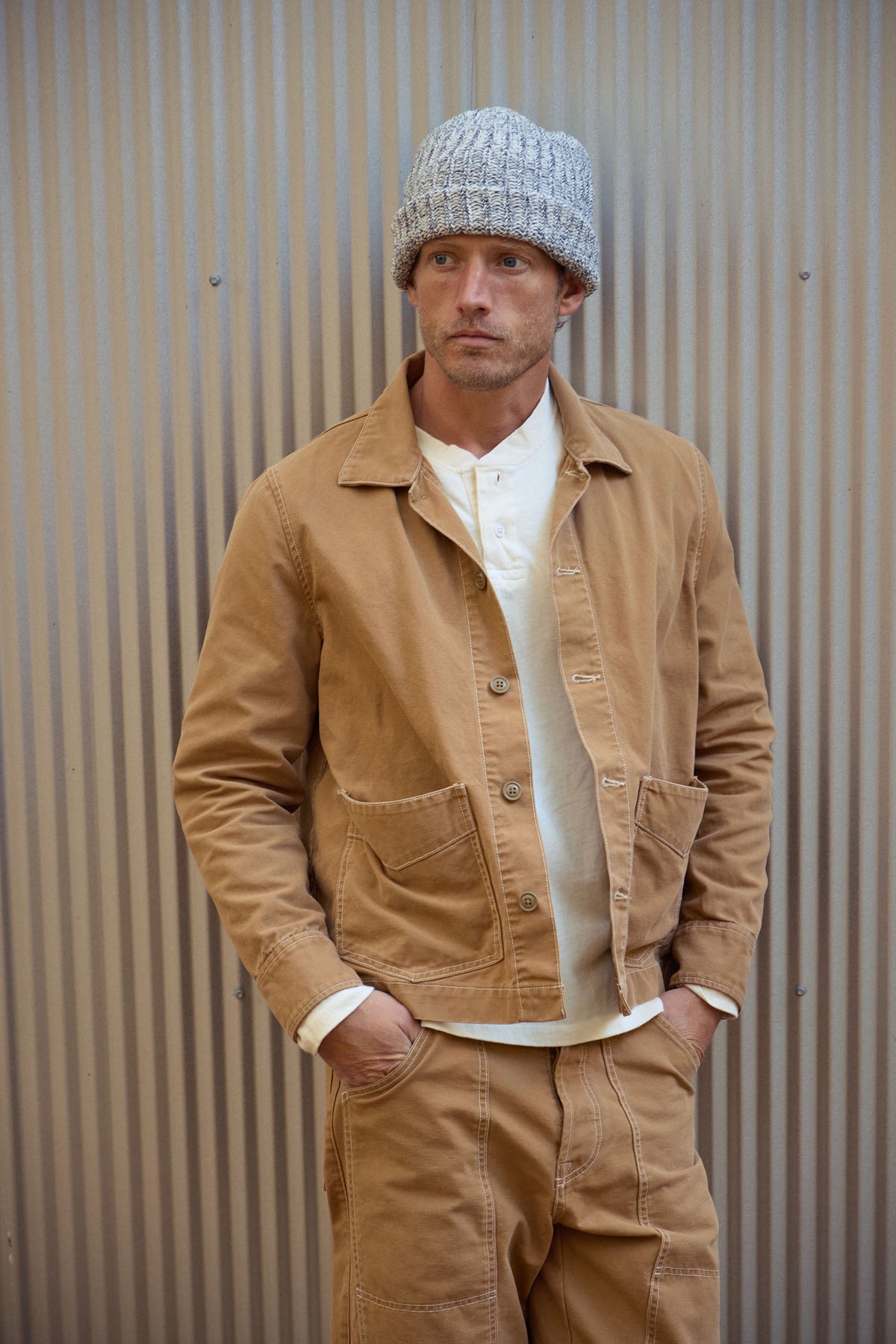 Brown canvas work jacket worn with knit beanie, chest pockets and button cuffs