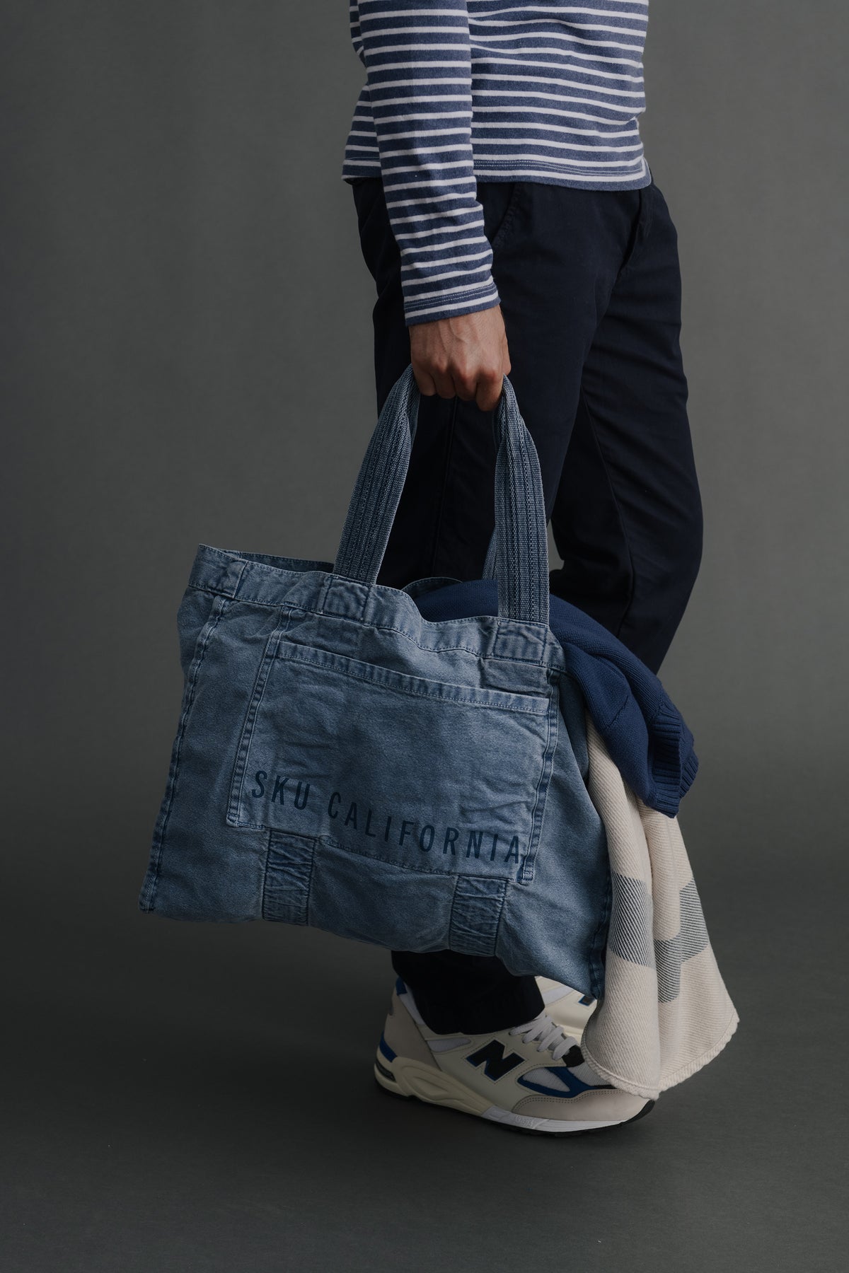 Blue denim tote bag carried on shoulder, front logo patch and reinforced seams